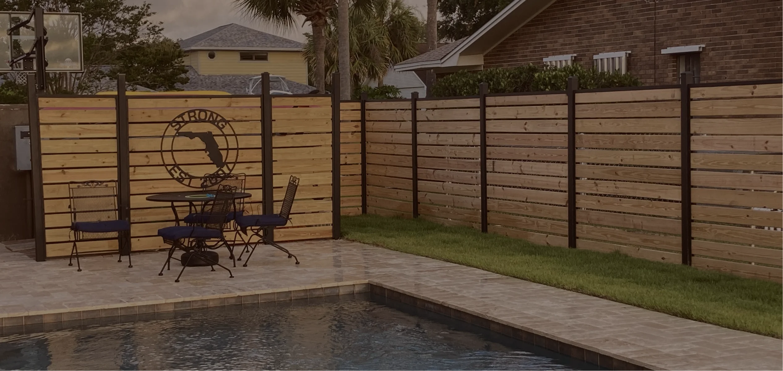 Backyard with a rectangular swimming pool, stone tile patio, metal table and chairs, and a wooden fence by slipfence with a circular Florida-shaped sign.