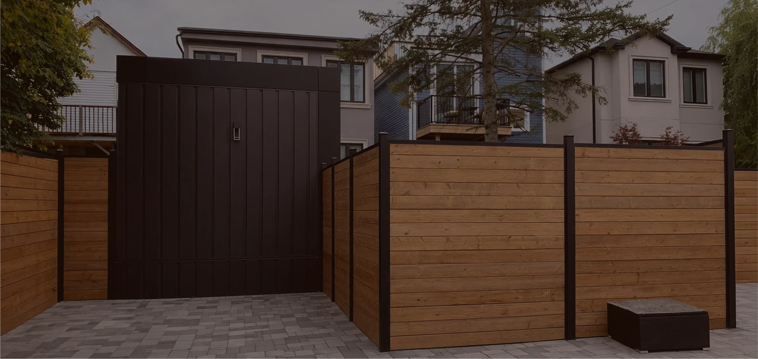 Modern outdoor wooden privacy fence by slipfence with black metal posts and gate, set on gray stone pavers in a residential area.