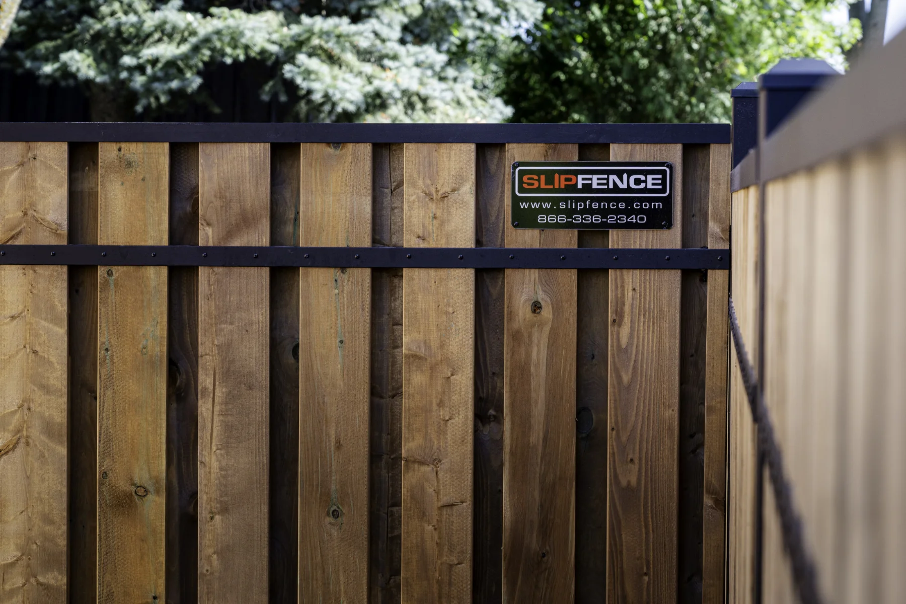 Fence by Slipfence with dark horizontal metal rails and a Slip Fence company sign displaying their website and phone number.