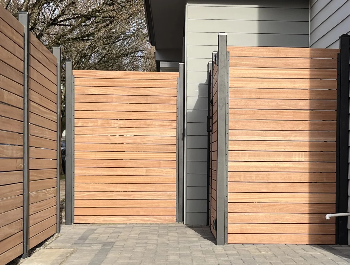 Modern wooden privacy fence panels by Slipfence with horizontal slats and black metal frames on a stone-paved path.